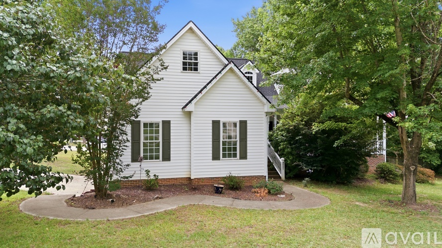 A white house with a grey roof surrounded by green trees.