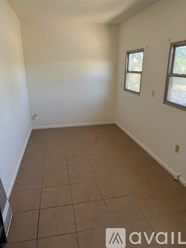 A room with tile flooring and two windows.