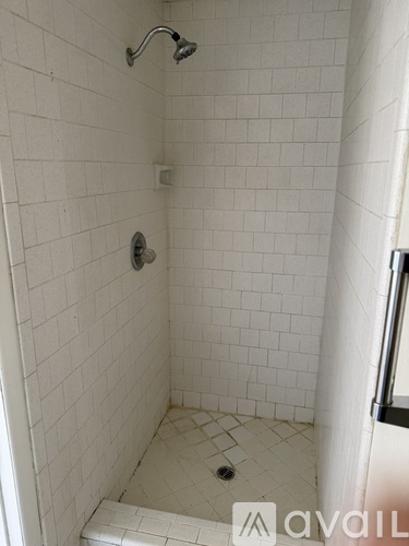 A white tiled shower with a drain in the middle.