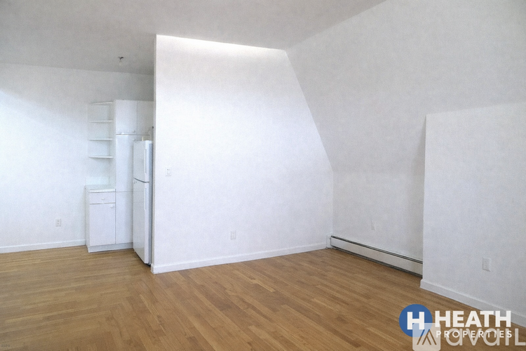 A white refrigerator sits in a room with wooden floors and white walls.