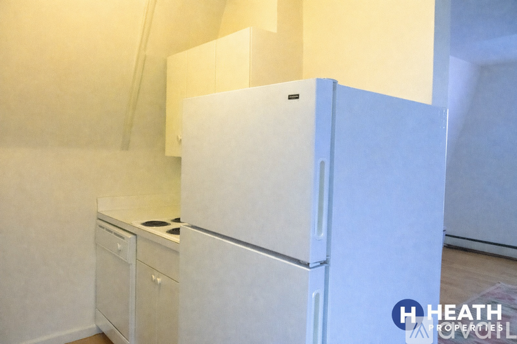A white refrigerator is in a kitchen with white cabinets.