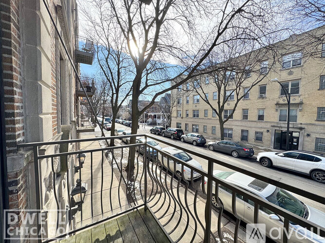 A balcony with a metal railing overlooks a street with cars and buildings.