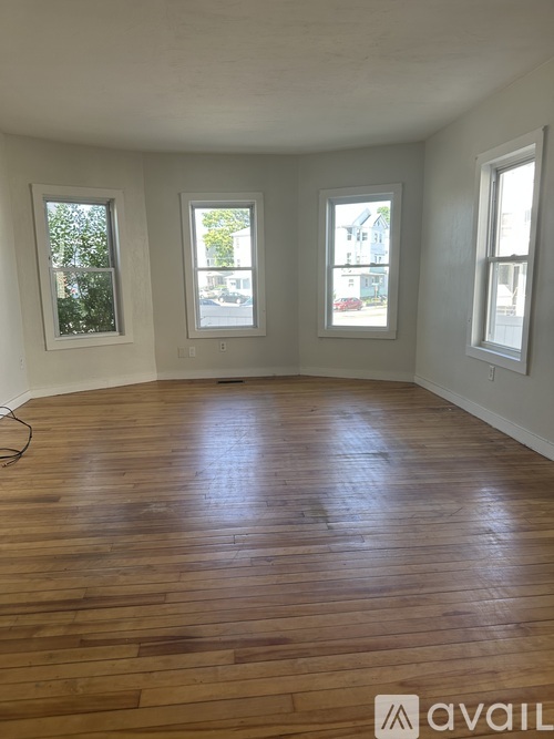 A room with wooden flooring and three windows.