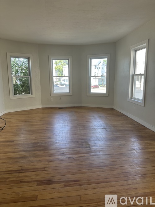 A room with wooden floors and three windows.