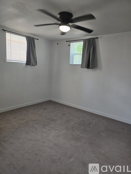 A room with a ceiling fan and two windows with curtains.