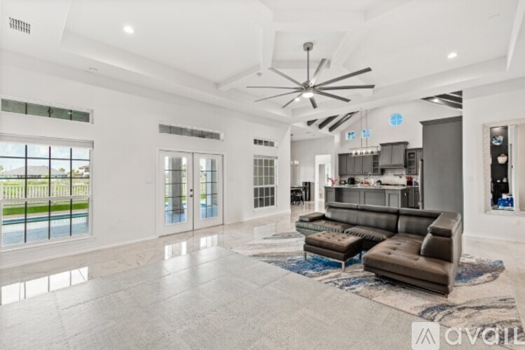 A spacious living room with a large sofa set and a kitchen area in the background.