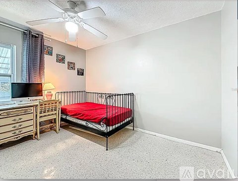 A bedroom with a red bed and a ceiling fan.