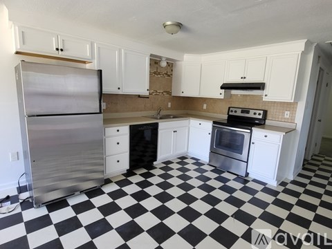 A black and white checkered floor in a kitchen with white cabinets and stainless steel appliances.