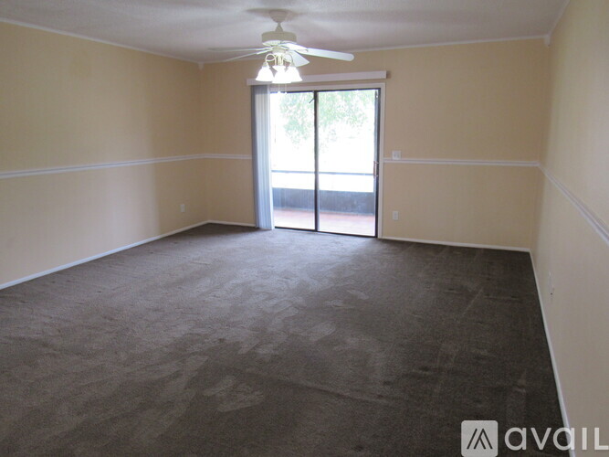 A room with a carpeted floor, a ceiling fan, and a sliding glass door leading to a balcony.