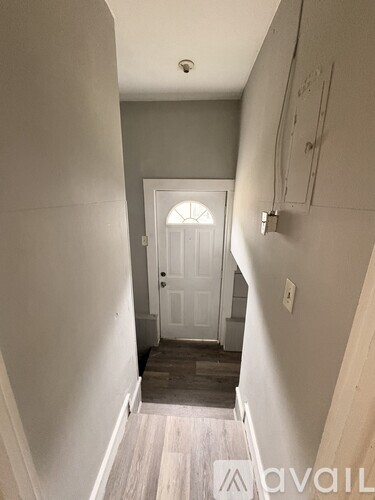 A hallway with a white door and wooden floors.