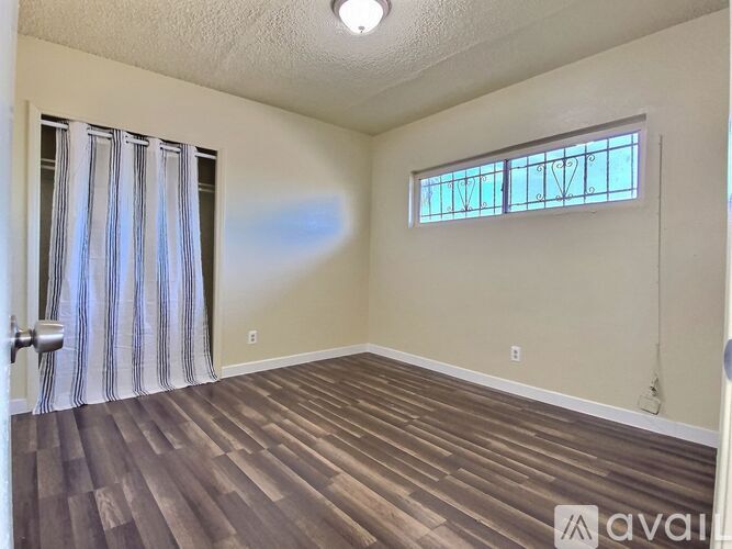 A room with wooden flooring and a window with a striped curtain.