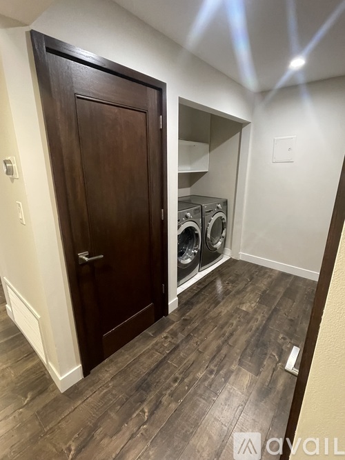 A room with a wooden floor and a brown door leading to a laundry area.