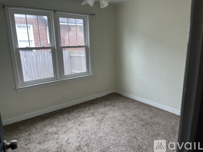 A room with a carpeted floor and a window with a view of a fence and a building.