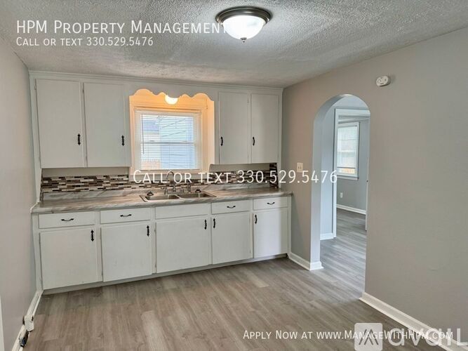 A kitchen with white cabinets and a window with a view of a backyard.