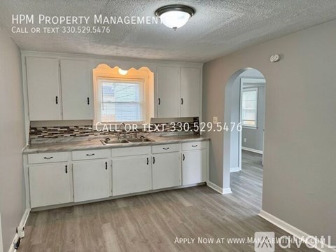 A kitchen with white cabinets and a window with a view of a backyard.
