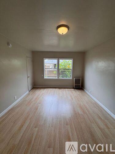 A room with wooden flooring and a window showing a view of a building and trees.