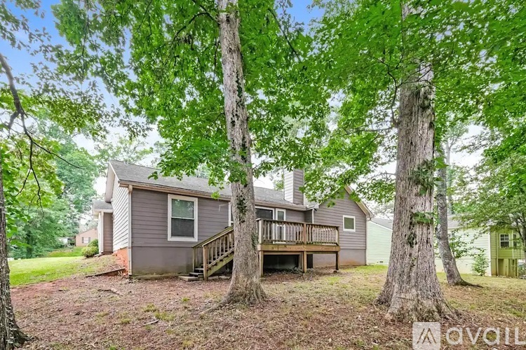 A house with a deck is surrounded by trees and is for sale.