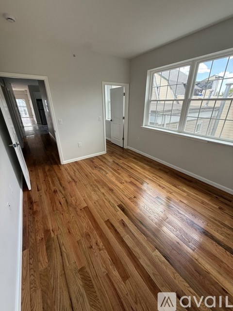 A room with wooden flooring and a window with a view of a building outside.