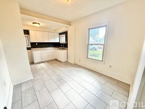 A white tiled kitchen and living room with a window.