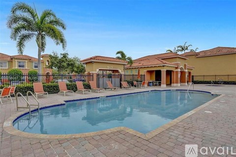 A swimming pool surrounded by a brick patio and lounge chairs with a house in the background.