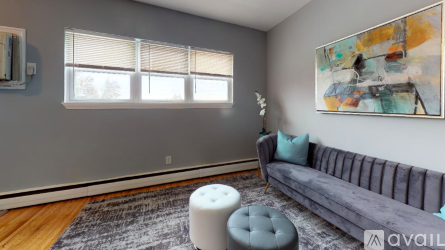 A grey couch with a blue pillow is in front of a painting in a room with a window.