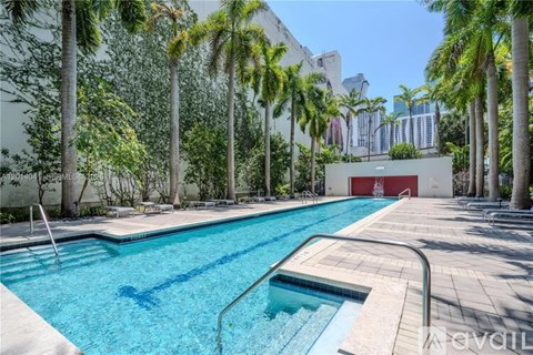A pool surrounded by palm trees and a red door in the background.