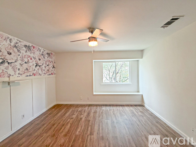 A room with a ceiling fan and a window with a view of trees.