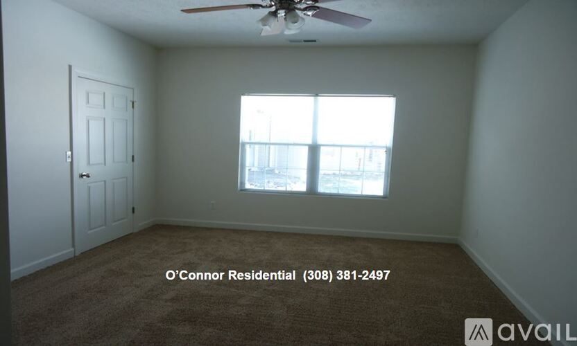 A room with a carpet floor, a ceiling fan, and a window with a view of a building.