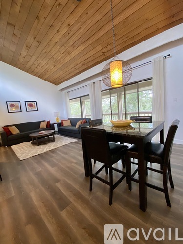 A wooden dining table with chairs and a couch in a room with wooden flooring and a wooden ceiling.