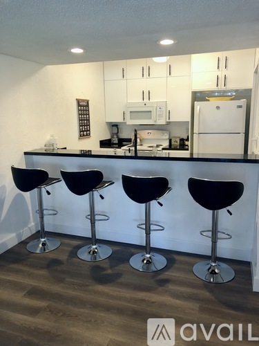 A kitchen with a bar area featuring four black bar stools.