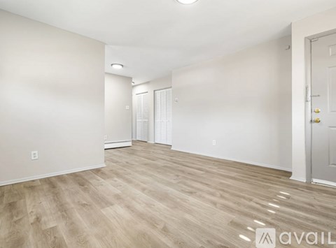A spacious room with light wood flooring and white walls.