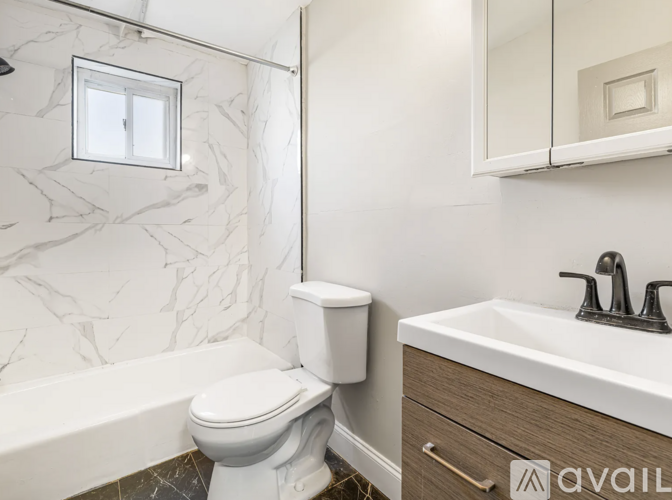 A white toilet sits next to a bathtub in a bathroom with marble walls.