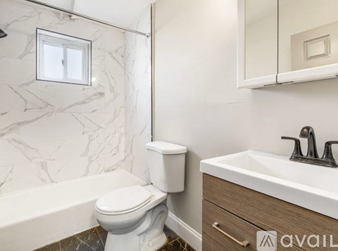 A white toilet sits next to a bathtub in a bathroom with marble walls.