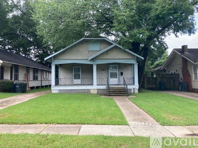 A blue house with a white porch and a green trash can.