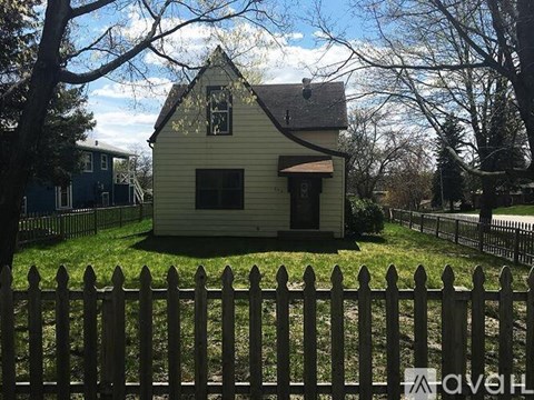 A small yellow house with a white picket fence in front.