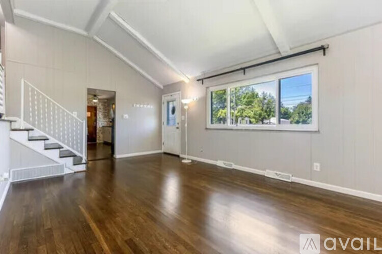 A spacious room with wooden floors and a staircase on the left side.