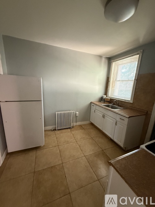 A kitchen with a white fridge, white cabinets, and a window with blinds.