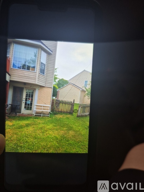 A person is holding a phone showing a residential area with houses and a lawn.