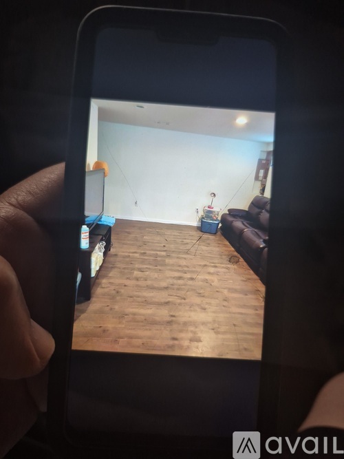 A person is holding a phone showing a room with wooden flooring and a couch.