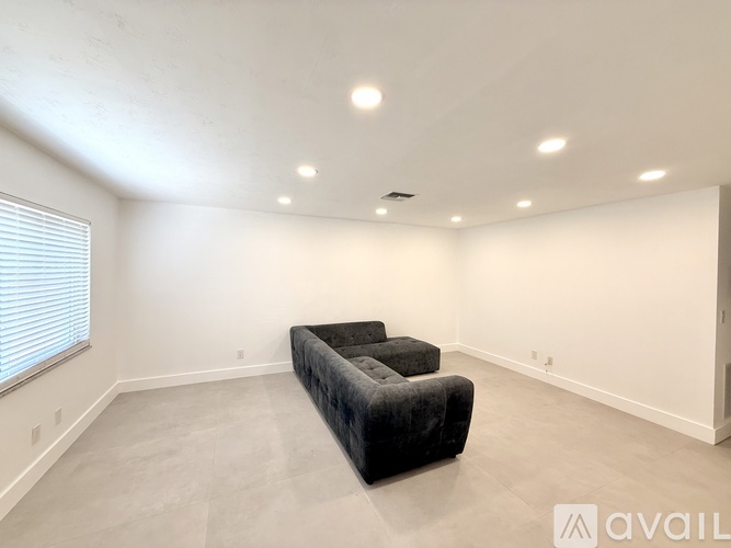 A spacious living room with a black couch and a window with blinds.