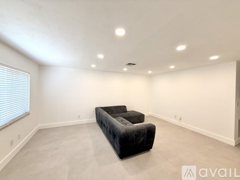A spacious living room with a black couch and a window with blinds.
