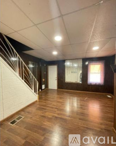 A spacious room with wooden flooring and a staircase with white railings.