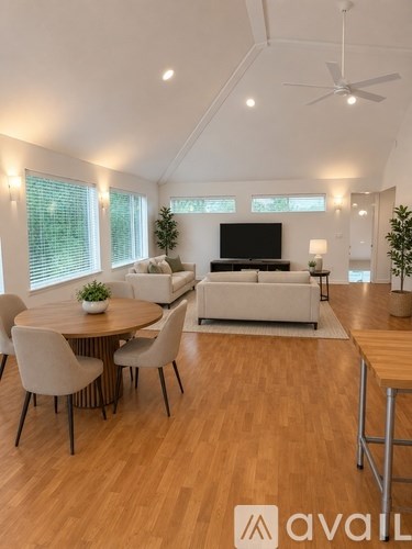 A living room with a white couch, a round table with four chairs, and a television.