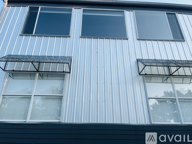 A building with a blue corrugated metal siding and three windows with white frames.