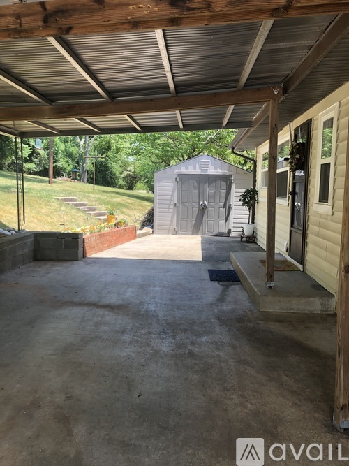 A covered patio area with a concrete floor and a shed in the background.