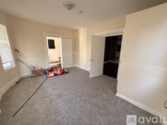 A room with a carpeted floor and white walls, with a door on the right and a window on the left.