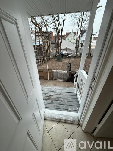 A view from inside a building looking out through a white door to a backyard with a deck and a tree.