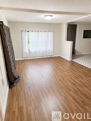 A room with wooden flooring and a window with white curtains.