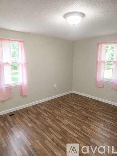 A room with wooden floors and two windows with pink curtains.