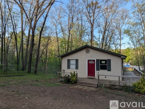 A small house with a red door is surrounded by trees.